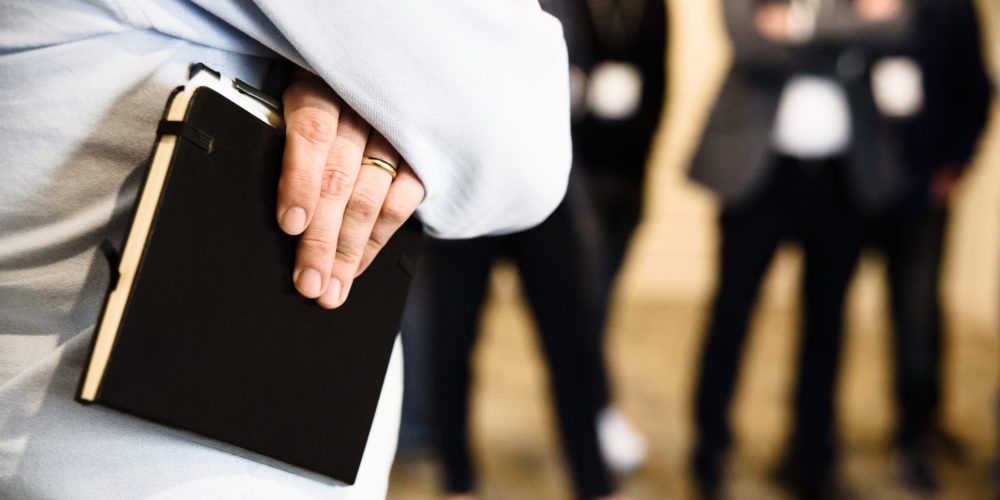Detail of the hand of a businessman holding a paper notebook.